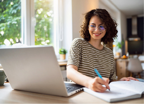 Woman smiling while writing on her notepad, next to her laptop