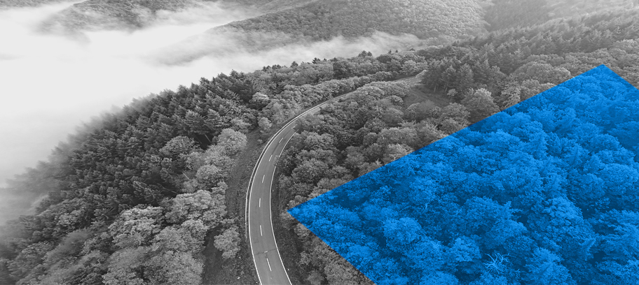 Industrial smokestacks combined with aerial view of a road winding through a forest.