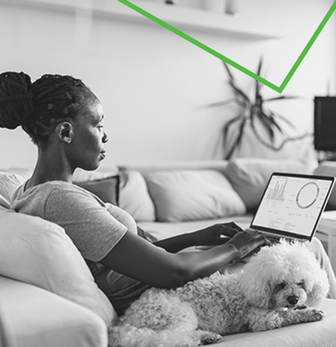 Woman sitting on a couch next to her dog, looking at a laptop screen showing investment charts..